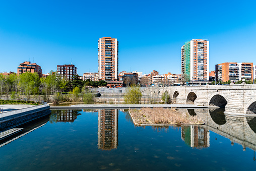 Madrid, Spain - March 14, 2021: Madrid Rio. Bridge of Segovia and Puerta del Angel quarter. Reflections of residential towers on water