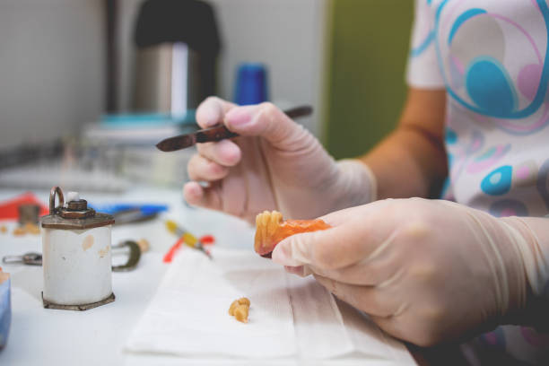 istock Close-up of a dental technician shaping a prosthesis tooth with a tool at work desk. 1324070823