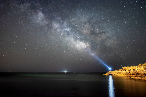 Person aims a flashlight toward the center of our home galaxy in front of the sea
