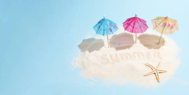 istock Summer beach vacation and travel concept, three multi-colored umbrellas on a sand island on a blue background in sunlight, banner. 1324074810