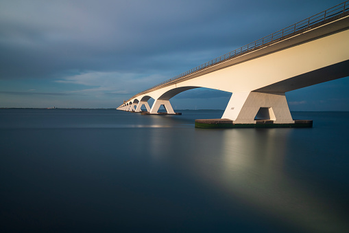 Beautiful long Zeeland bridge leading over the sea in Holland. Photo at sunset long time. There are nice blue clouds in the sky.