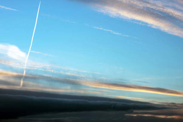 Natural landscape background. Evening sunset sky with clouds with white stripes from passed by air plane.