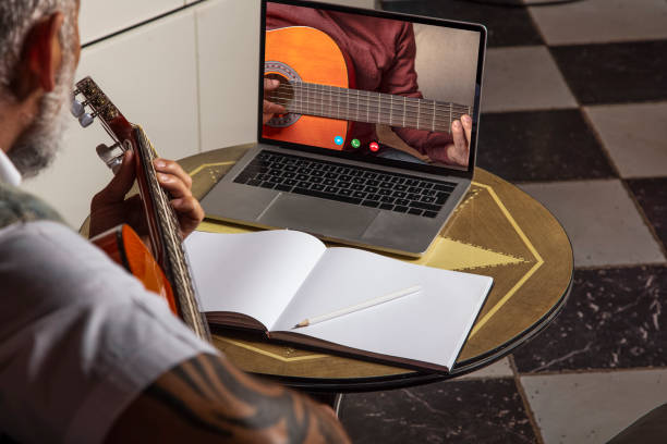istock Man playing acoustic guitar and watching online classes on laptop while practicing at home..Online training, online classes. 1324081241