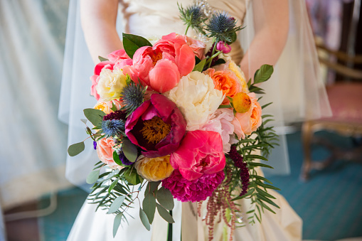 The bride holds her bridal bouquet in front of her waist against a white background.