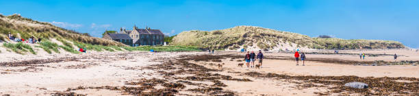 northumberland ludzi spaceru na bamburgh plaży wydmy panorama uk - bamburgh beach zdjęcia i obrazy z banku zdjęć