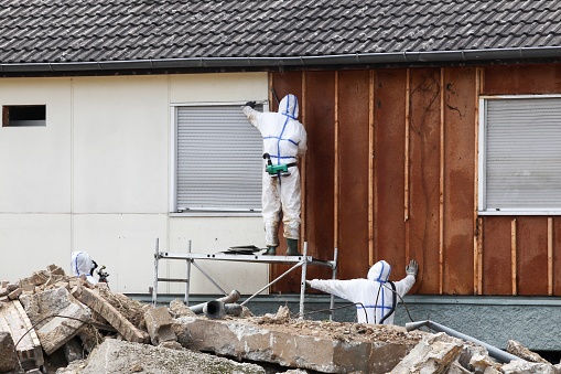 Professionals in protective suits remove asbestos on a wall