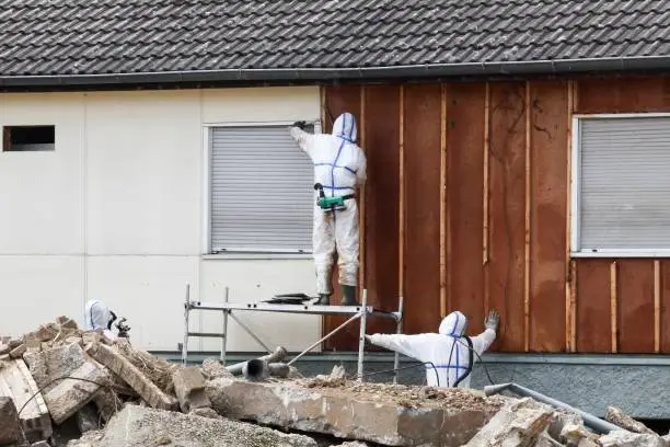 Photo of Professionals in protective suits remove asbestos on a wall