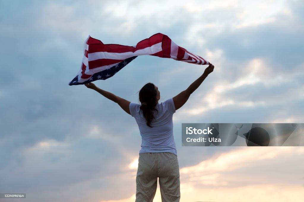 a woman with an American flag on the ocean at sunset. Independence Day. The United States celebrates July 4. 40-44 Years Stock Photo