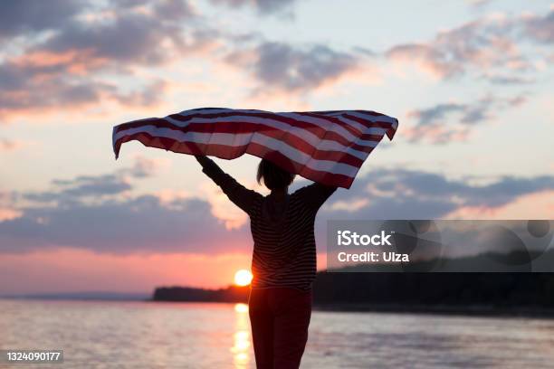 A Woman With An American Flag On The Ocean At Sunset Independence Day The United States Celebrates July 4 Stock Photo - Download Image Now