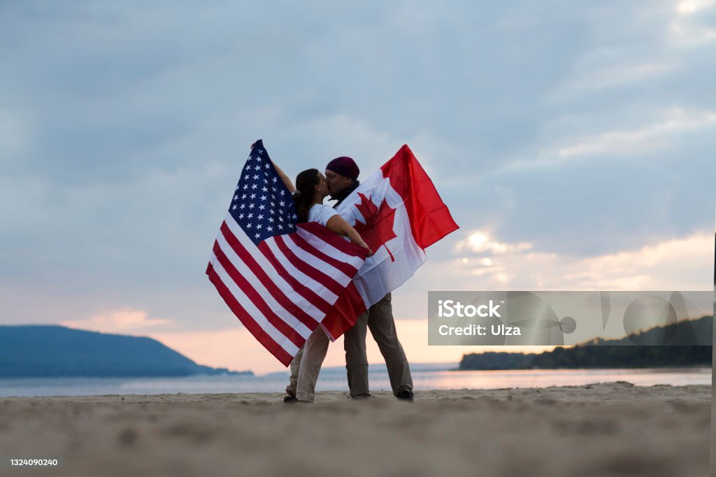 Independence Day. The United States celebrates July 4.
woman and man with flags of America and Canada on the ocean at sunset. 40-44 Years Stock Photo