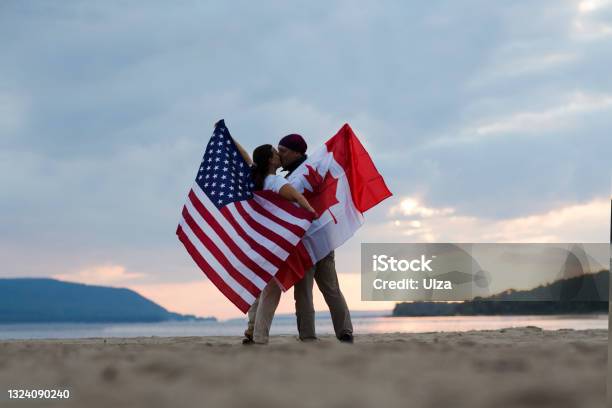 Independence Day The United States Celebrates July 4 Woman And Man With Flags Of America And Canada On The Ocean At Sunset Stock Photo - Download Image Now