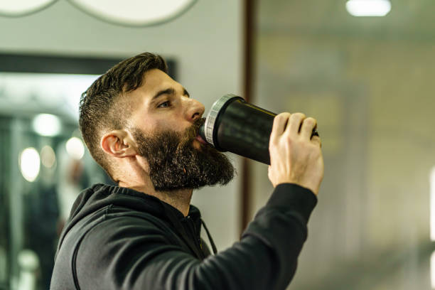 istock Young adult man with beard drinking bottle supplement shake in training at gym side view copy space real people 1324091898