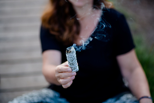 Woman with dark hair and black top holds incense (sage) in her hand to expel negative energy
