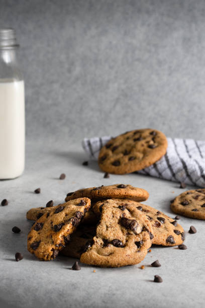 schokoladen-chip-cookies mit einer flasche milch und einer serviette im hintergrund - bakery food defocused table stock-fotos und bilder