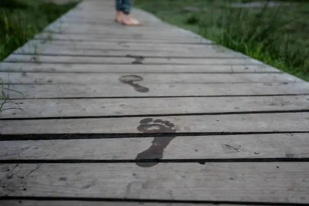 many footprints from wet feet on a boardwalk. Women's feet are at the edge of the picture