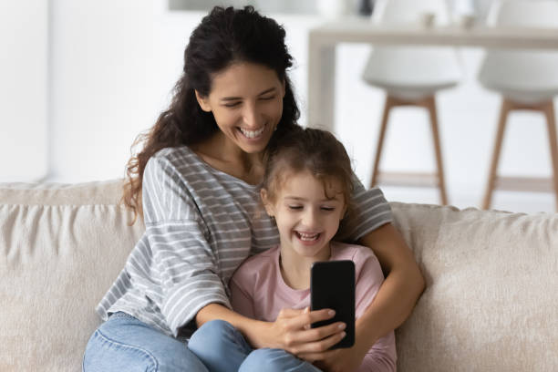 istock Smiling Latin mother and small daughter laugh using smartphone 1324096496