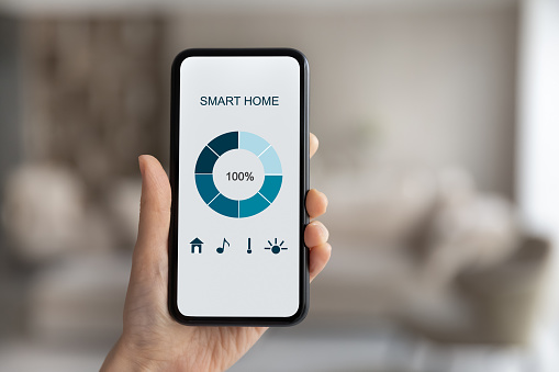 Close up of woman hold smartphone gadget use smart home application system on electronic device. Female renter tenant with cellphone check smarthome control panel. Modern technology concept.