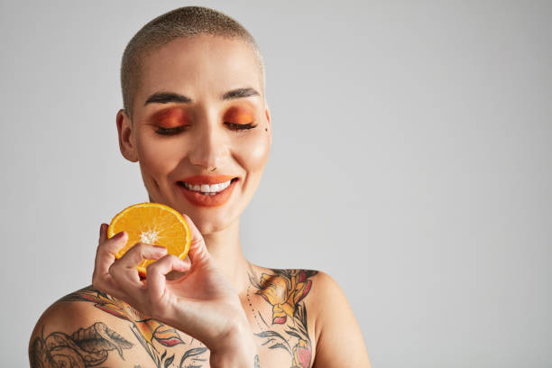 scatto in studio di una bella giovane donna in posa con arance su sfondo grigio - human lips orange lipstick human mouth foto e immagini stock