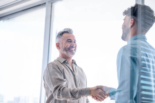 Two businessmen shaking hands. Two businessmen shaking hands. They are wearing casual business clothes and standing in an office boardroom. They are smiling and happy. There is a window behind them casual job interview stock pictures, royalty-free photos & images