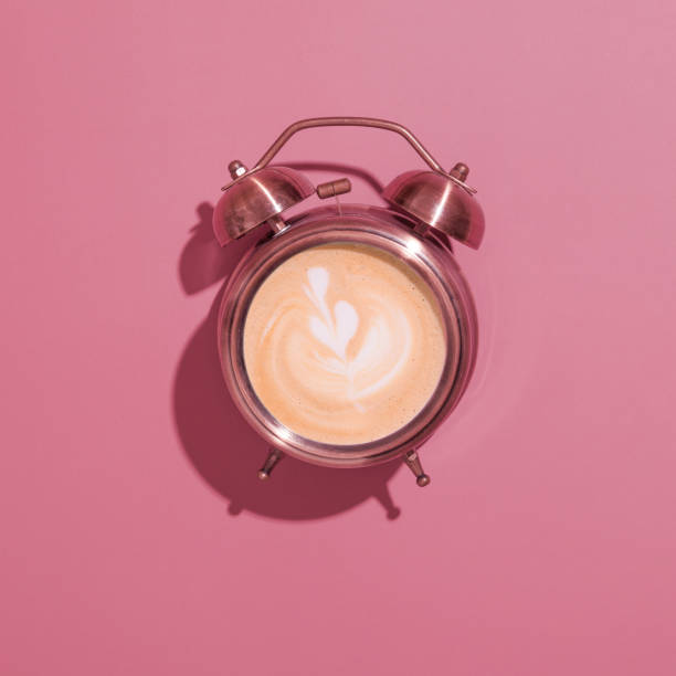istock Alarm clock on with foamy coffee and pattern. Hard shadows. Morning rise with coffee for breakfast concept 1324102543
