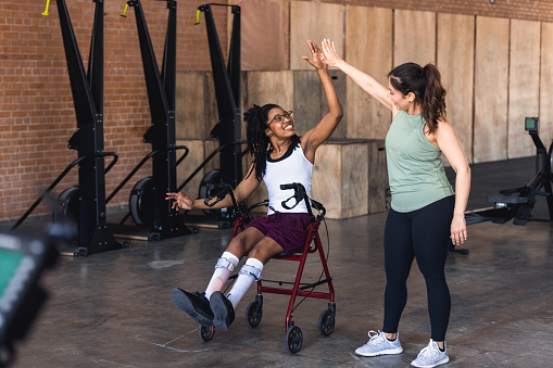 At the fitness center, the young adult woman gets a high five from her teacher after the workout.