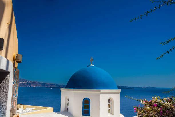 Oia, Santorini Island, Greece - July 4, 2018: This is a view with the Silk 100% store sign on the left side and a church in the middle. On the Aegean Sea there are two ships and cruise ships.