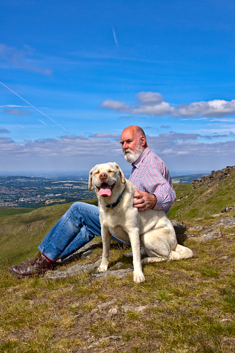 Man in his 70s resting with his dog in the rolling hills above Glossop, Derbyshire.