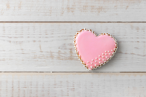 heart shaped cookie decorated by pink glaze on a wooden white background with copy space