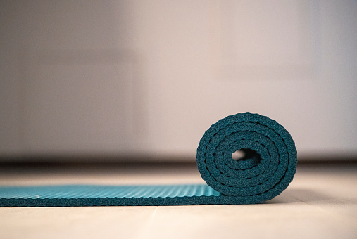 A blue yoga mat is slightly unrolled on a wooden floor.