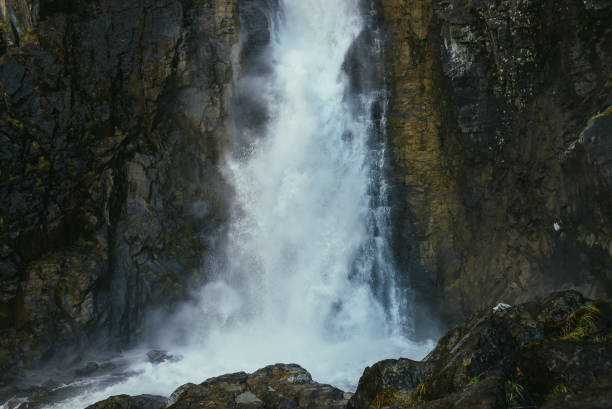 istock Atmospheric minimal landscape with vertical big waterfall on rock mountain wall. Powerful large waterfall in dark gorge. Nature background of high vertical turbulent falling water stream on wet rocks. 1324123258