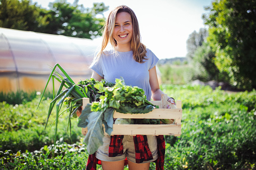 An image portraying a happy farmer. She's proudly posing with a basket full of greens she harvested and can't wait to put into every meal during the next week.