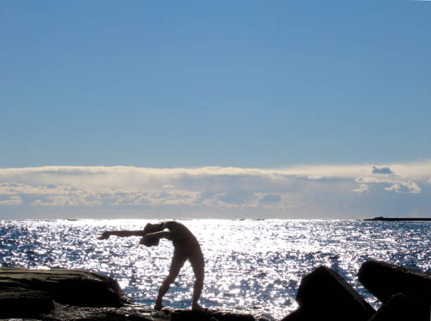 naked man sunbathing on rocky beach - yoga nudist silhouette naked imagens e fotografias de stock