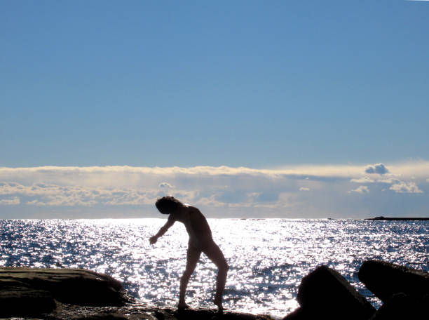 nackter mann sonnenbaden am felsigen strand - yoga nudist silhouette naked stock-fotos und bilder