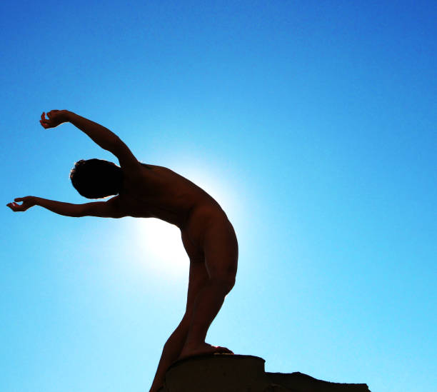 naked man sunbathing on rocky beach - yoga nudist silhouette naked imagens e fotografias de stock