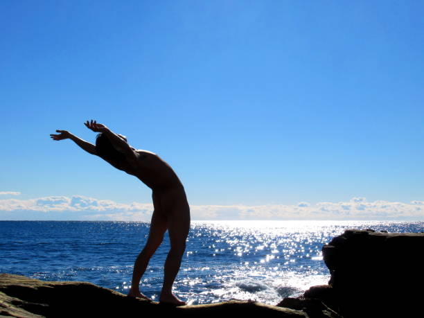 naked man sunbathing on rocky beach - yoga nudist silhouette naked imagens e fotografias de stock