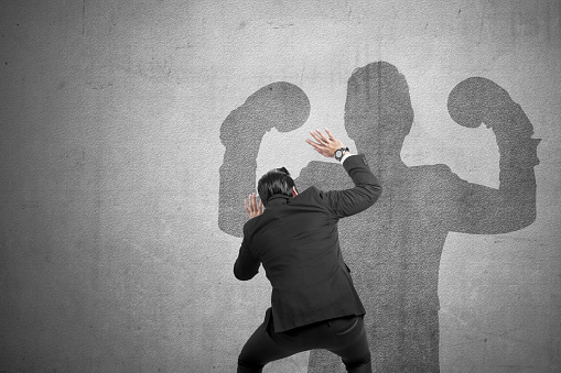 Rear view of Asian businessman afraid of muscular shadow on the wall