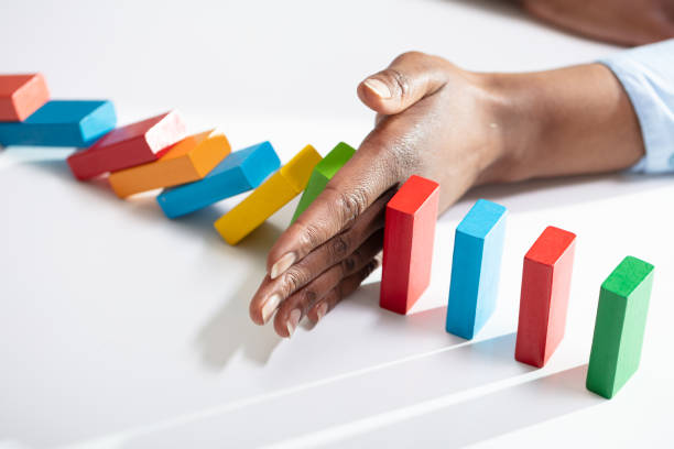 Businesswoman Stopping Dominoes On Desk Close-up Of A Businesswoman Hand Stopping Colorful Dominoes From Falling On Office Desk hand stopping dominos stock pictures, royalty-free photos & images