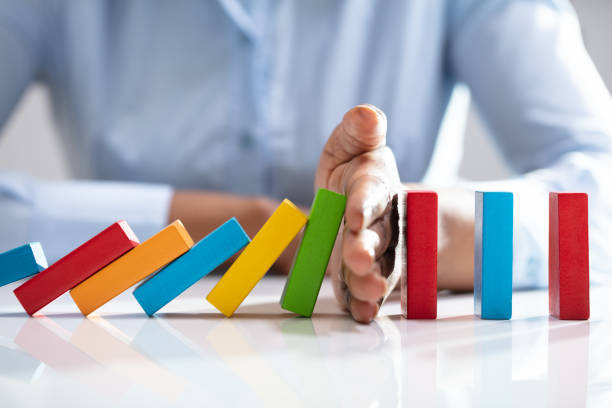 Businesswoman Stopping Dominoes On Desk Close-up Of A Businesswoman Hand Stopping Colorful Dominoes From Falling On Office Desk prevention stock pictures, royalty-free photos & images