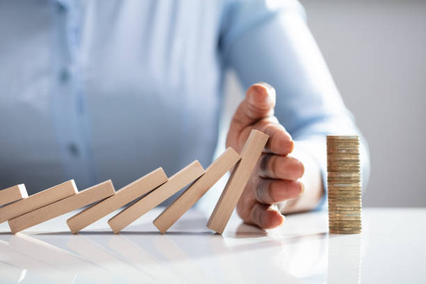 Person Stopping Dominos From Falling With Stacked Coins Human Finger Stopping Dominos From Falling With Stacked Coins On White Desk hand stopping dominos stock pictures, royalty-free photos & images