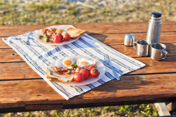 Breakfast in nature. Fried eggs with bacon, fried toast and hot coffee from a thermos. Selective focus