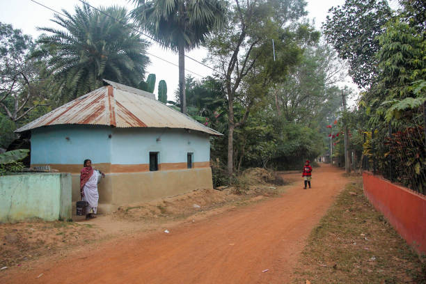 Shantiniketan, West Bengal, India - January 2015: A dirt road going past a rustic mud hut with slanted roofs in a village in the outskirts of Bolpur.