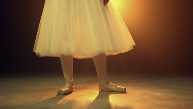 Young dancer putting on ballet shoes indoors. Ballerina tying pointe on stage.