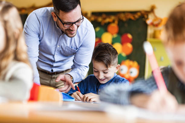 istock Young happy professor assisting his elementary students on a class at school. 1324167830