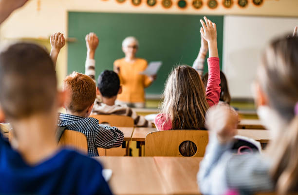 istock Back view of students raising their hands to answer the teacher's question on a class. 1324167966