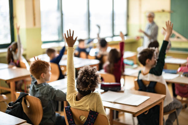 istock Rear view of elementary students raising hands on a class. 1324168825