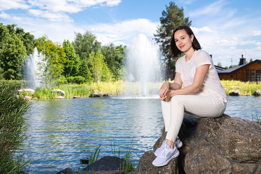 Beautiful woman sits on a stone near the lake in the park.