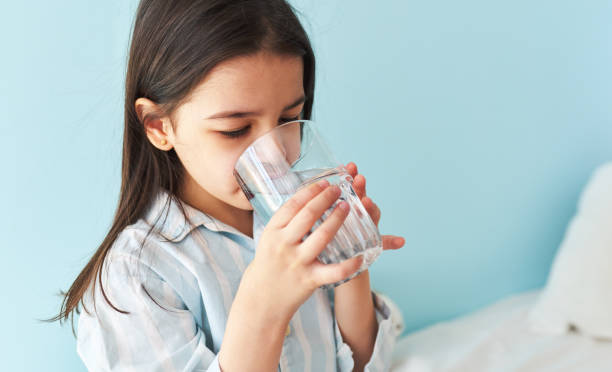 Portrait of a little girl drinking fresh water in the bed at home. Cute preschool kid holding glass of pure water in the morning. Healthy lifestyle concept. stock photo