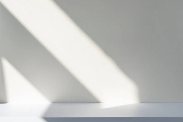 istock Sunlight and abstract shadows on the wall and white desk. Silhouette of lines on blank surface, mockup, space for text. 1324171732