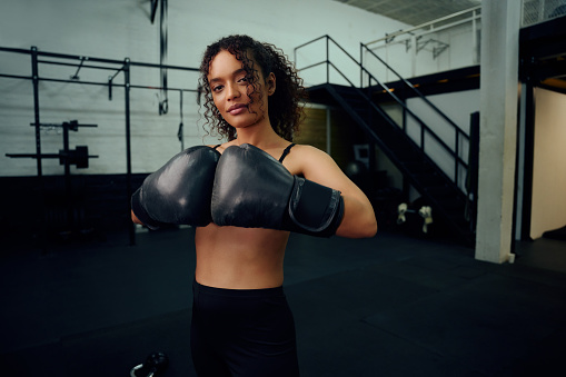 Female boxer training at the gym with boxing gloves on. Mixed race female holding boxing gloves in air. High quality photo. High quality photo