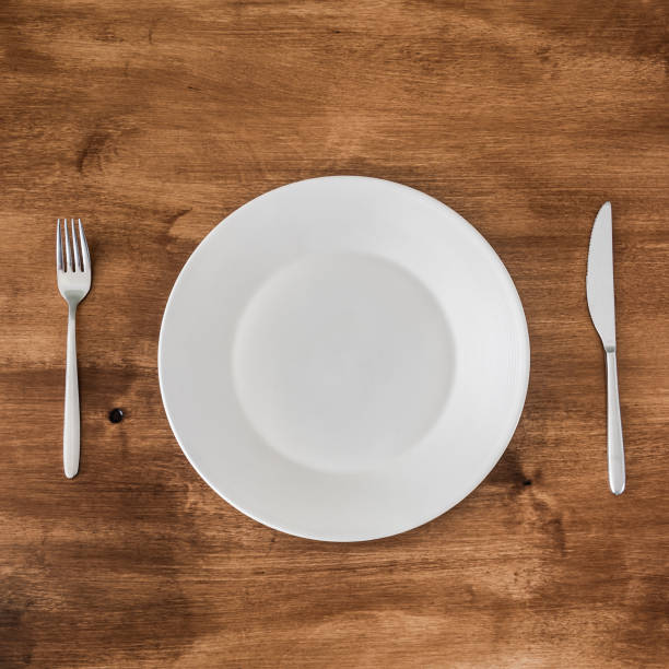 istock empty plate with knife and fork on wooden background 1324173440